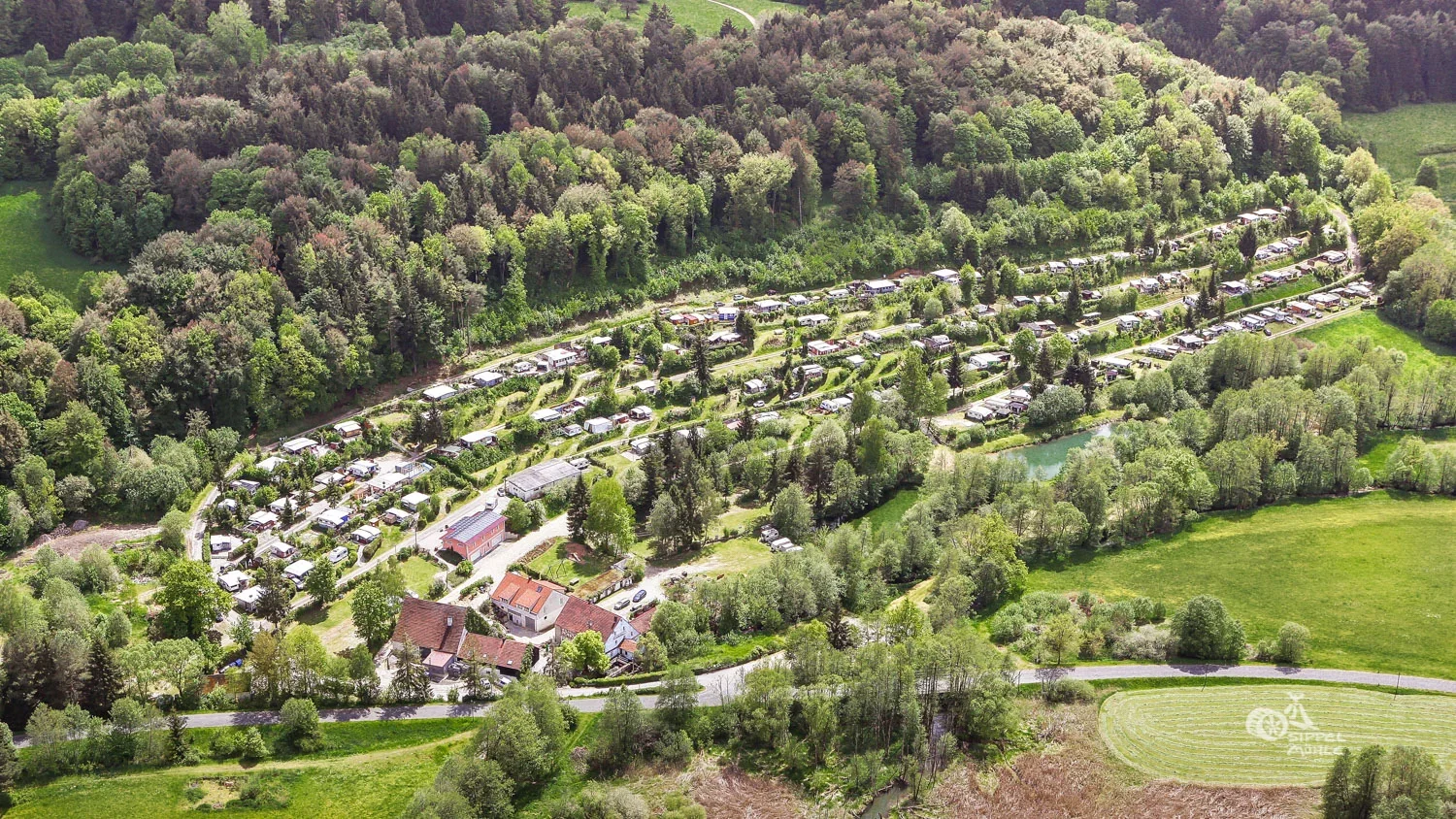 Luftaufnahme der terrassierten Anlage zwischen Wald und Wiesen.