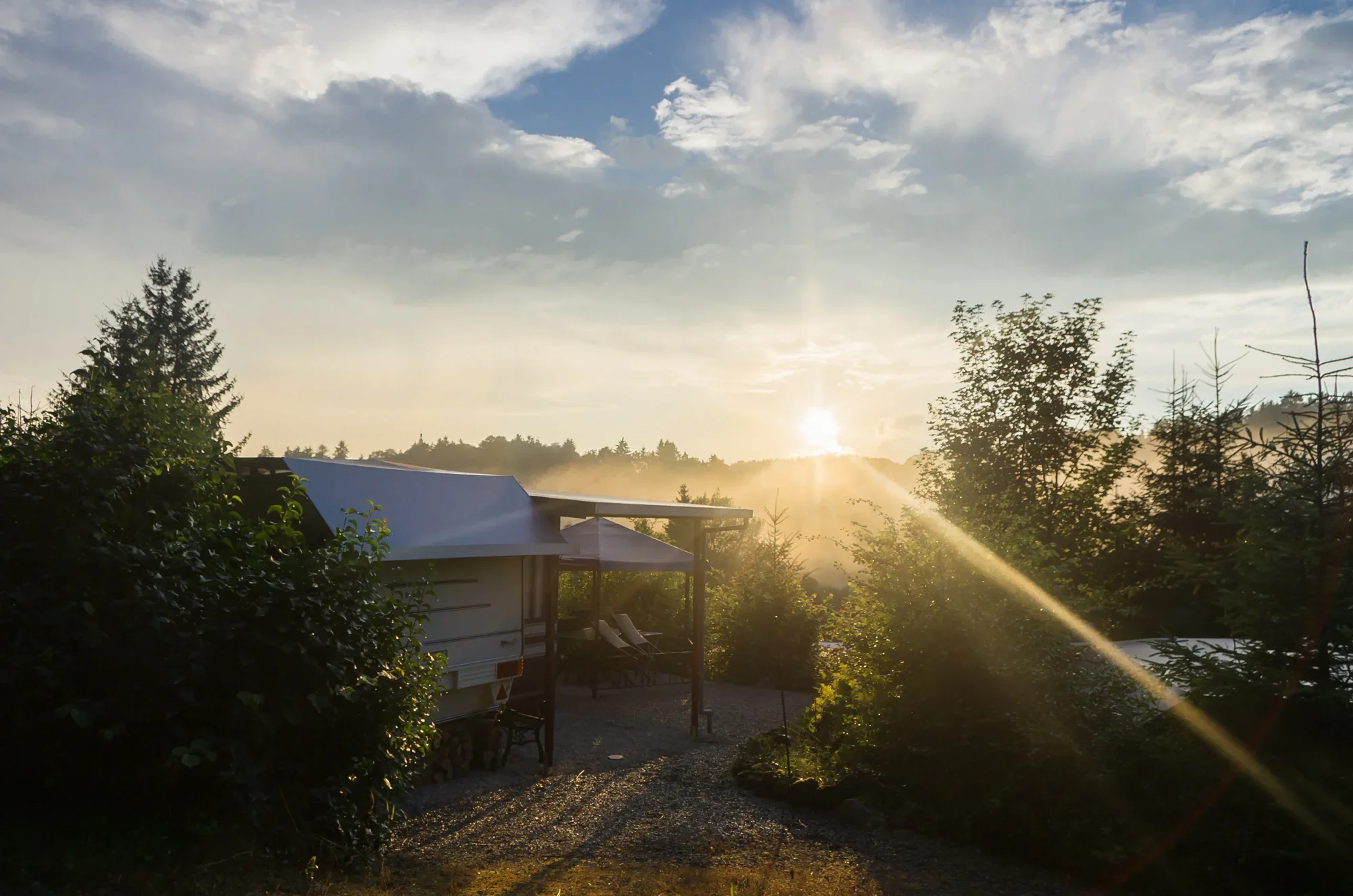 Tief stehende Sonne über den Hecken und Wohnwagen des Campingplatzes.