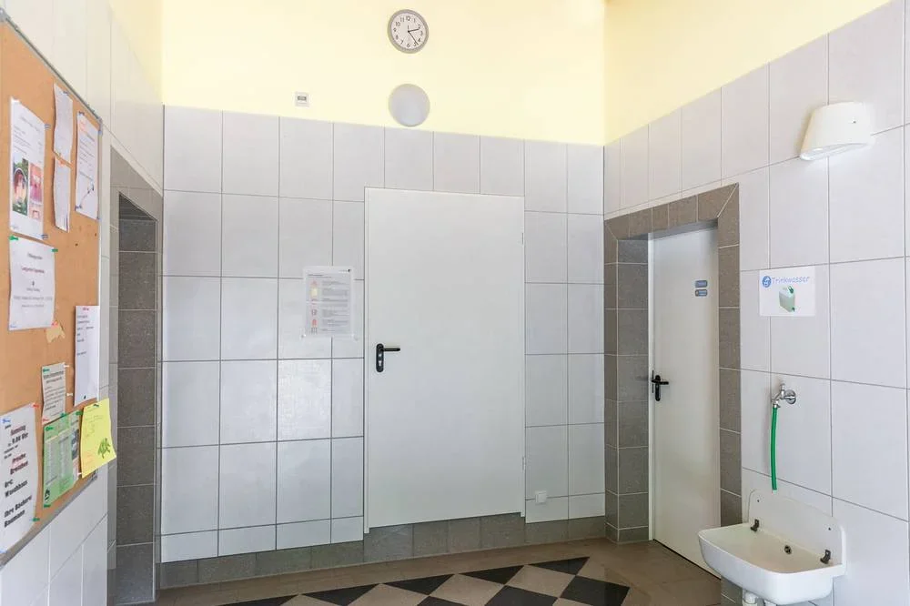 Eingangshalle mit Zugängen zu den Damen- und Herrenbereichen und einer Trinkwasserstelle.