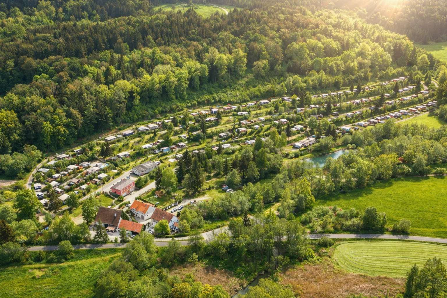 Panoramablick auf die terrassierten Stellplätze des Campingplatzes Sippelmühle, umgeben von Wald und Wiesen.