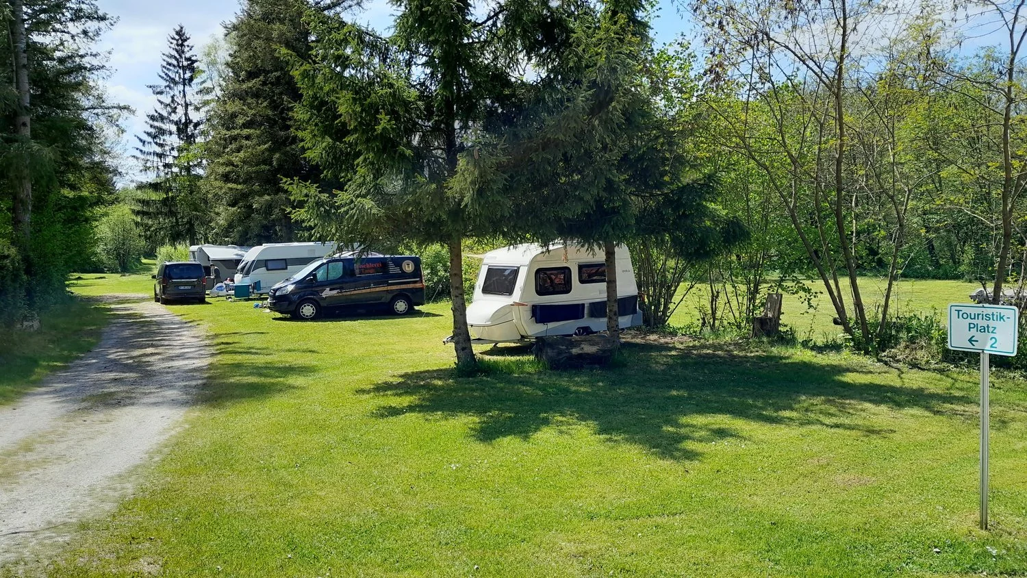 Wohnwagen und Reisemobile zwischen Bäumen am Urlaubsplatz.